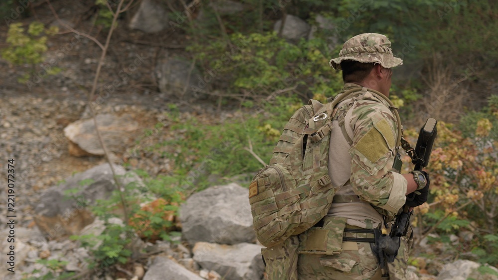 Fototapeta premium A soldier in full combat gear patrols through a rugged, rocky wilderness on a reconnaissance mission, showcasing tactical readiness and strategic surveillance.