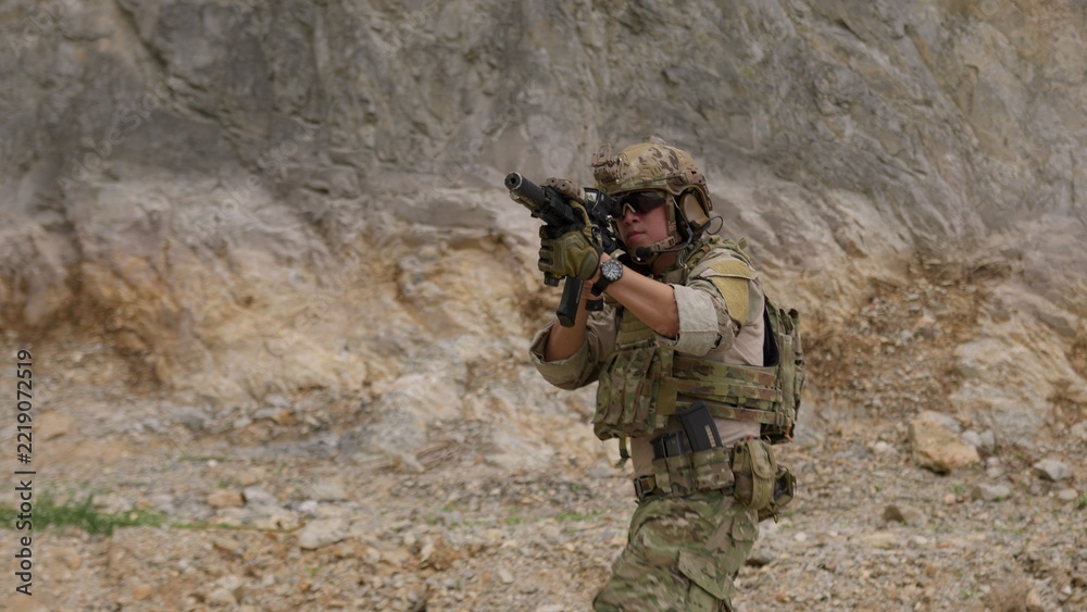 Fototapeta premium A special forces operator in full combat gear advances cautiously through a rocky, hostile environment while aiming his assault rifle on a tactical security patrol.
