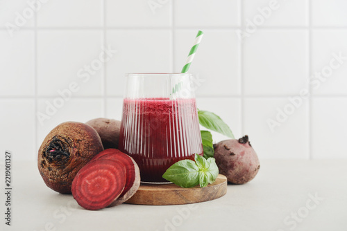Beetroot juice in a glass with a striped paper straw, served with raw beetroot and fresh basil