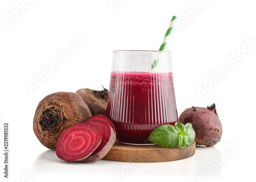Beetroot juice in a glass with a striped paper straw, served with raw beetroot and fresh basil
