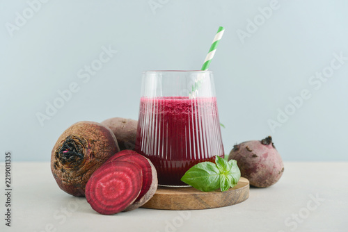 Beetroot juice in a glass with a striped paper straw, served with raw beetroot and fresh basil