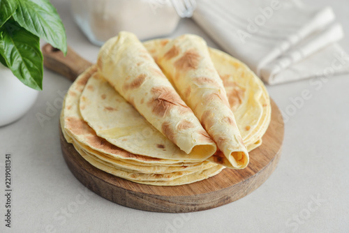 Stack of lavash or chapati flatbreads on a wooden cutting board, with a jar of flour, fresh basil