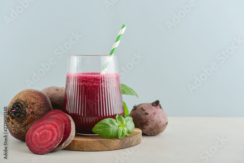 Beetroot juice in a glass with a striped paper straw, served with raw beetroot and fresh basil