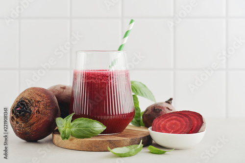 Beetroot juice in a glass with a striped paper straw, served with raw beetroot and fresh basil