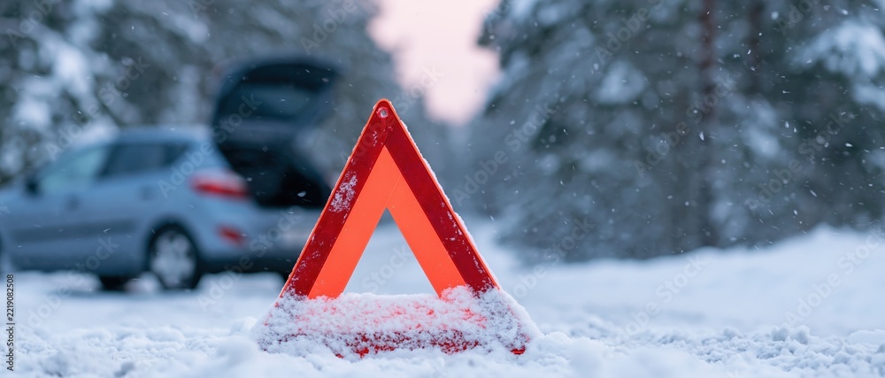 Naklejka premium Red emergency warning triangle in snow near broken-down car on winter road