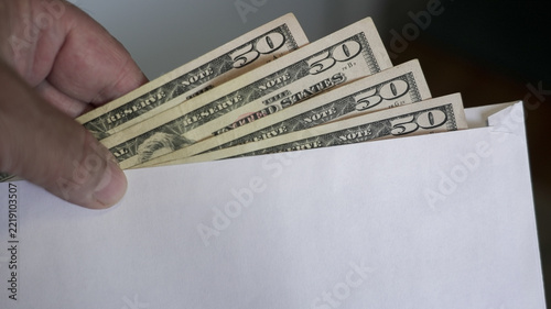 Hand Holds US Fifty Dollar Bills Emerging From White Envelope Offering Financial Transaction Concept