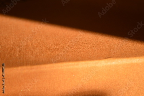 Abstract background featuring a warm orange textured surface with dramatic diagonal light shadows