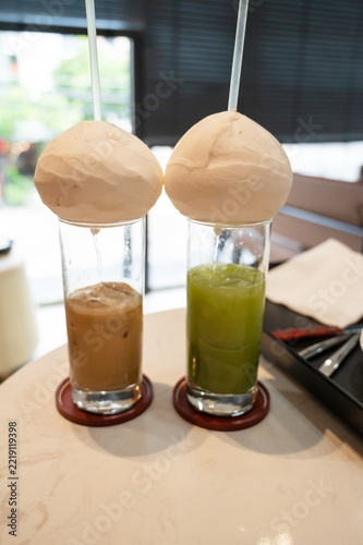 Creative presentation of iced coffee and iced matcha in tall glasses into which coconut water flows from the coconut, served in a modern cafe in Vietnam