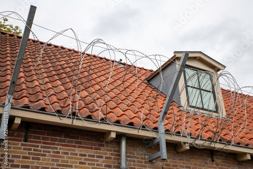 Barbed Wire Fence Across Red Tile Roof With Dormer Window Symbolizing Security And Protection
