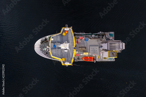 Aerial view of a salmon slaughter boat on dark water, featuring processing equipment, a small orange rescue boat, and industrial machinery in Liabygda, More og Romsdal, Norway.