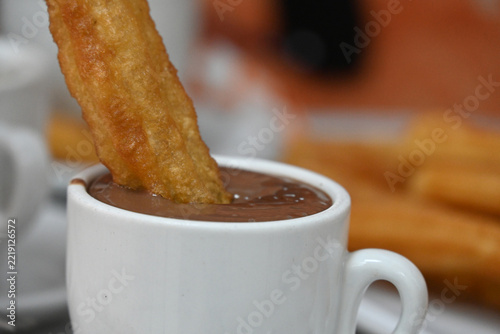 churros with hot chocolate and coffee, traditional golden churros served with a cup of thick hot chocolate and coffee on a cafe table, with a hand dipping a churro into chocolate