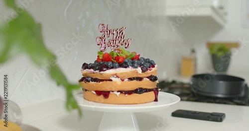 On start, camera is moving and shifting focus, showing three-layer cake on countertop with berries