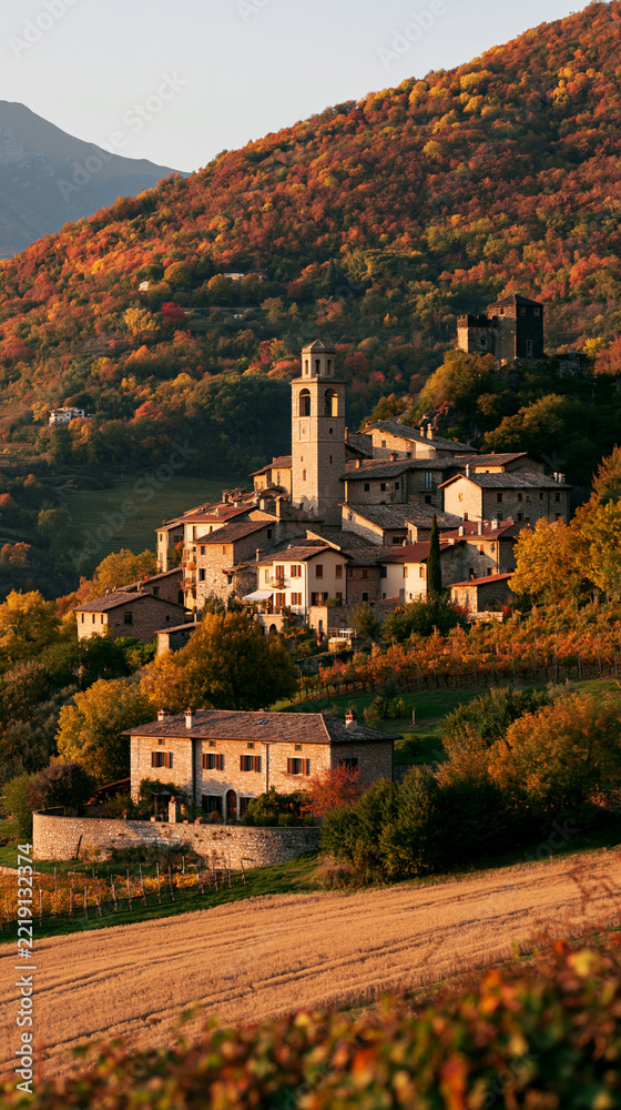 Fototapeta premium a picturesque village nestled amidst a hillside covered in autumn foliage. The village features a mix of traditional stone and stucco structures, including a church with a bell tower.