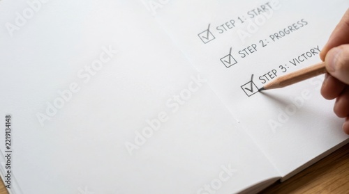 A hand holding a pencil checks off the final step labeled Victory on a list success