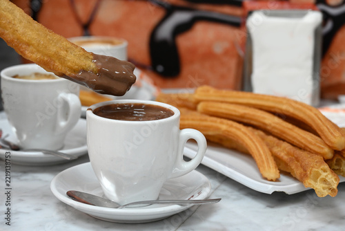 churros with hot chocolate and coffee, traditional golden churros served with a cup of thick hot chocolate and coffee on a cafe table, with a hand dipping a churro into chocolate