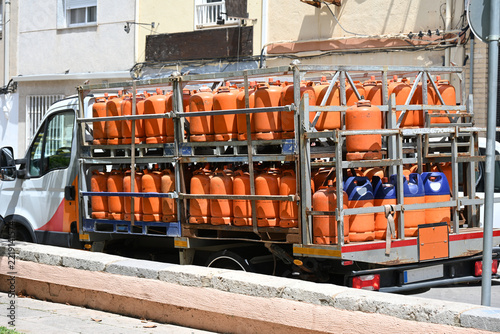 truck transporting orange gas cylinders, delivery truck loaded with numerous orange liquefied petroleum gas cylinders parked on a residential street, showing transportation and distribution of bottled