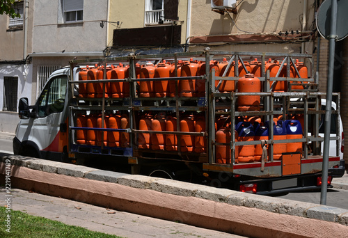 truck transporting orange gas cylinders, delivery truck loaded with numerous orange liquefied petroleum gas cylinders parked on a residential street, showing transportation and distribution of bottled