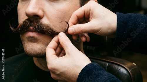 Barber hands styling and shaping client handlebar mustache in barbershop closeup