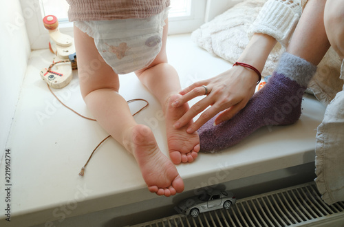 Close-up of a mother touching her toddler's feet on a windowsill