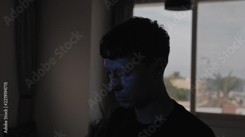 Emotionally drained man walking into frame and standing with a downcast gaze, expressing sadness and inner emptiness, dark cinematic home interior with blue light and large copy space on the right