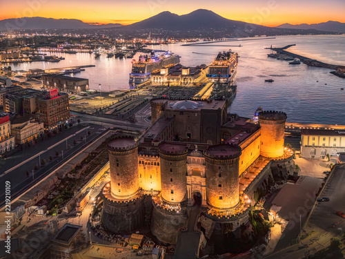 Sunrise over castle Nuovo in Naples, Italy. NAPLES, ITALY - OCTOBER 3, 2026: Aerial illuminated view of Castle Nuovo or Maschio Angioino at sunrise with cruise ships in the port and Mount Vesuvius in 