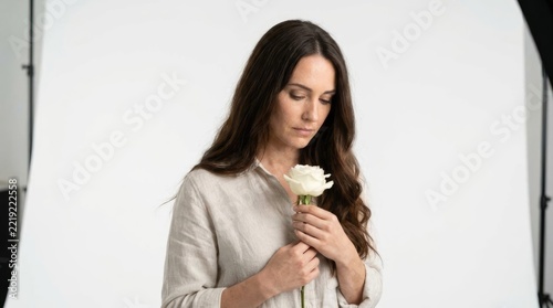 Sad woman holding white rose in minimalist studio