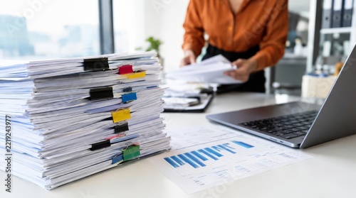 Stacks of paperwork piling on office desk with employee working