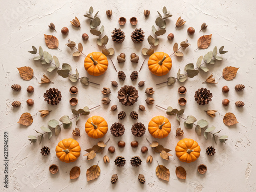 Autumn mandala flat lay with orange mini pumpkins, pinecones, acorns, dry leaves, and eucalyptus on beige texture background