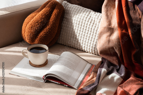Cozy scene with coffee and book on sofa warm blanket and textured pillows
