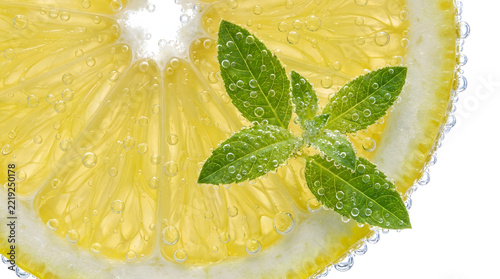 Fresh lemon slice with green mint leaves submerged in sparkling water