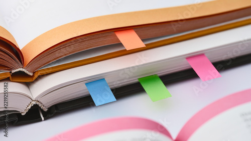 Selective focus view of stacked open textbooks with vibrant colored sticky flags indicating important sections.