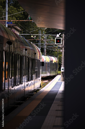 Fotografie Regional passenger train rounding a curve at the Merano station platform, facing a red signal