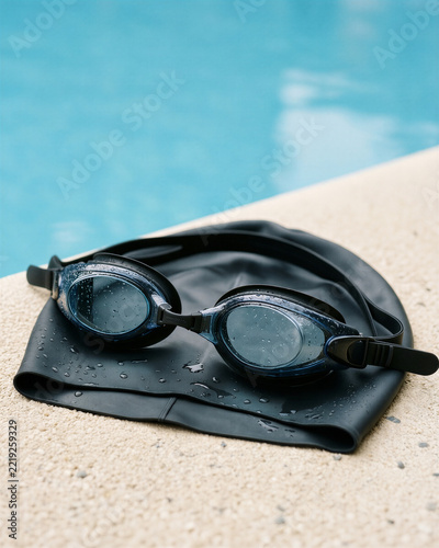 A swimming cap and goggles on a plain pool bench