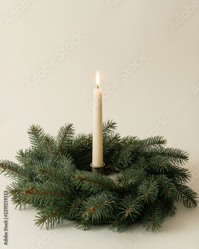 An unlit taper candle beside a simple evergreen wreath