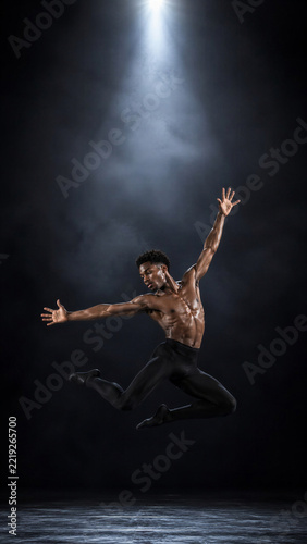 Athletic male ballet dancer jumping in dark studio, perfect for performing arts promotion, theater poster design, and motivational fitness marketing campaigns