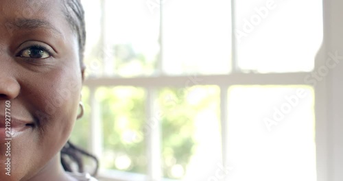Mid-adult woman responding to camera cue, holding gaze, widening smile near paned window