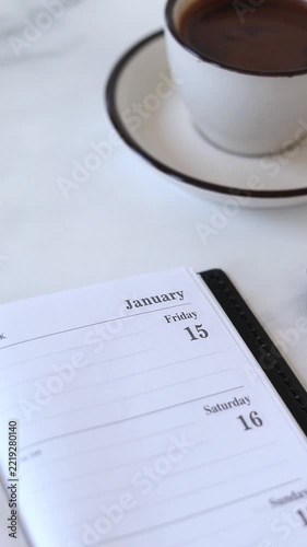Flipping page on January first new year calendar in a notebook with coffee cup on a desk. Vertical video.