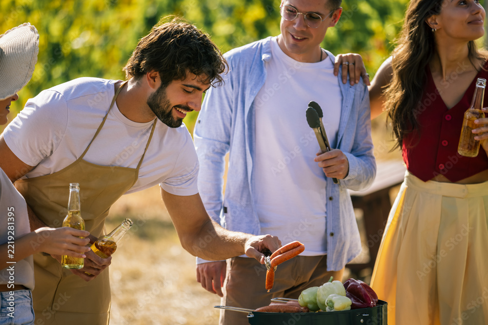 Fototapeta premium Man grilling food while friends gather around in a vineyard