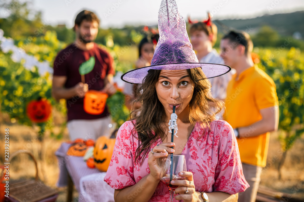 Fototapeta premium Woman in witch costume holding a drink at a Halloween vineyard party