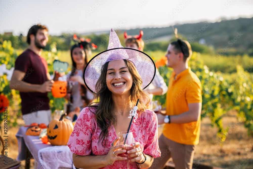 Fototapeta premium Smiling woman in witch costume holding a drink at an outdoor Halloween party