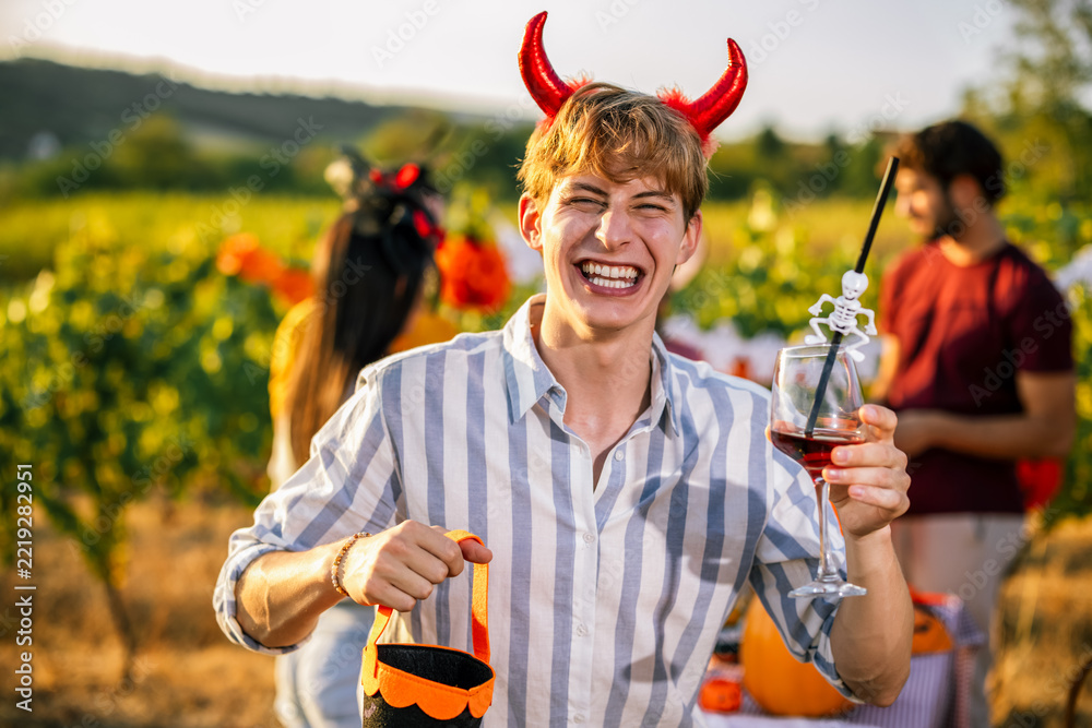 Naklejka premium Smiling man wearing devil horns and holding a wine glass at Halloween