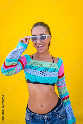 Happy young woman pulling down sunglasses on yellow background