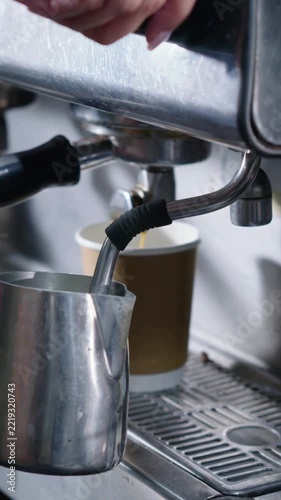 Vertical video: Steaming milk jug and wand, hand turning valve, frothing milk for latte at cafe bar