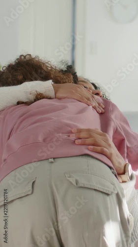 Vertical video: Reaching woman in white top hugging woman in pink sweatshirt at home for comfort