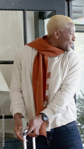 Vertical video: Opening black door man pulling suitcase into entry wearing rust scarf for reunion