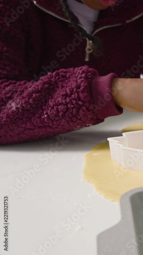 Vertical video: Moving fleece kid after adult tap pressing cookie cutter at table to cut