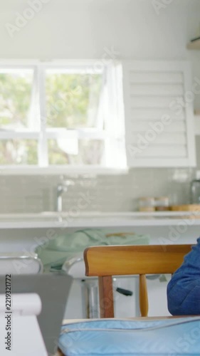 Vertical video: Entering kid in denim jacket doing homework at kitchen table with pencil