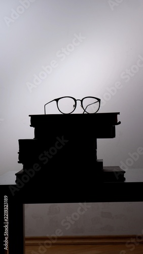Stack of books creating a silhouette shape with round reading glasses resting on top, representing education, wisdom, learning, study, knowledge, intelligence, and vision for the future