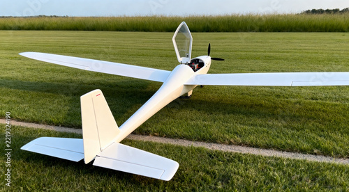 White remote-control glider model aircraft on grass field with open canopy and propeller