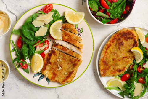 Chicken Milanese with lemon wedges and a salad of arugula, cherry tomatoes, and Parmesan
